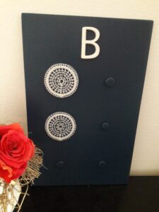The braille letter b made from white lace on a black background. The braille dots are designed in a shape roughly resembling a tightly woven spider web. Above the braille letter there is a white roman letter B. On the left of the letters there is a red rose.