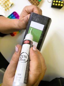 A person uses the Perlen Pen ‘Zen Pen’ in color 101 Snow to write on the spine of a folder.