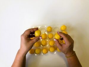 On a plastic structure, there are 24 small yellow surprise eggs. They contain different materials that make different sounds. Hands hold two eggs while trying to find a matching pair.