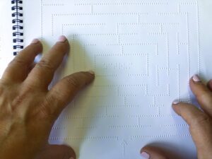 Fingers are used to find the way through a labyrinth of raised Braille dots. There is an arrow at the bottom showing the start of the path.
